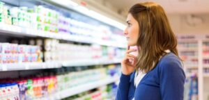 Small business owner looking overwhelmed by a wall of supermarket shelves.