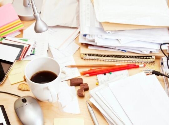 Messy desk with laptop, sticky notes and phone notifications showing scattered marketing activity and lack of focus.